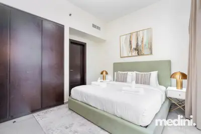 Bedroom with green upholstered headboard, two gold lamps, and a built-in wardrobe