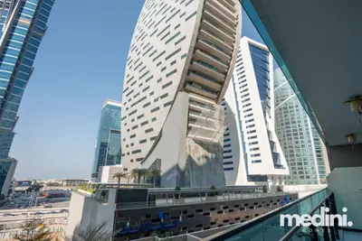 Balcony view of a sculptural white tower and surrounding urban buildings