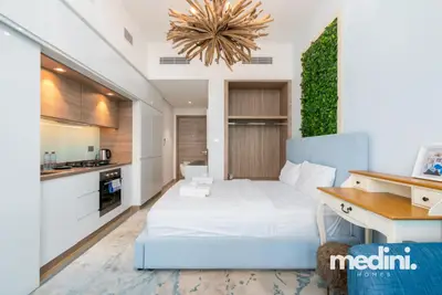 Wide view of the studio showing the bed, built-in kitchen, and ceiling pendant