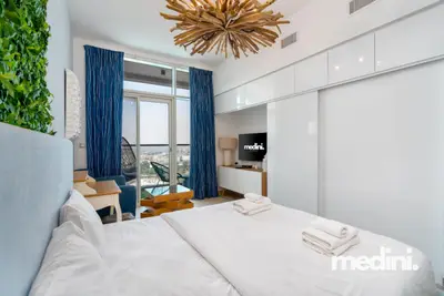 Studio with blue-curtained balcony doors, a sculptural ceiling light, and white wardrobe