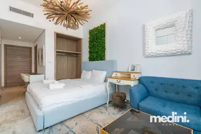 Studio bedroom area with blue upholstered headboard, blue sofa, and a moss wall panel