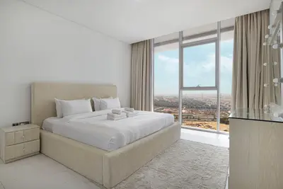 Bedroom with a beige upholstered headboard, folded towels, and floor-to-ceiling city view
