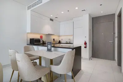 Dining area with four chairs at a marble-top table, open kitchen and entrance door beyond