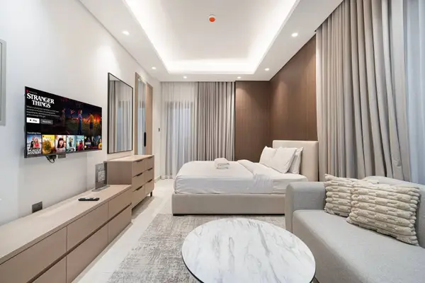 Living and sleeping area with flat-screen TV on and neutral-tone sofa and rug
