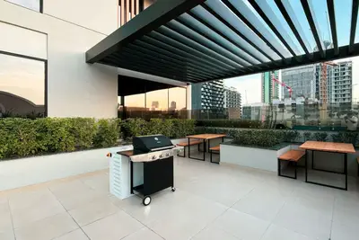 Rooftop terrace with a barbecue grill, wooden benches, and a pergola overhead