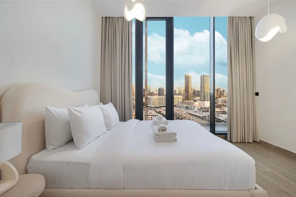 Bedroom with a double bed, white linens, and a wide city-view window