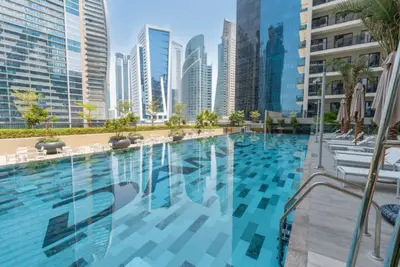 Outdoor pool with sun loungers, palm trees, and glass tower reflections in water