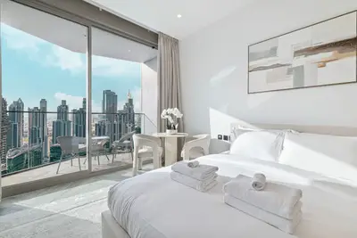 Bright bedroom with king bed, folded towels, and full-height glass balcony doors