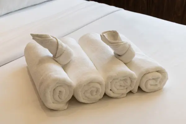 Four rolled white towels arranged in a row on a white bed