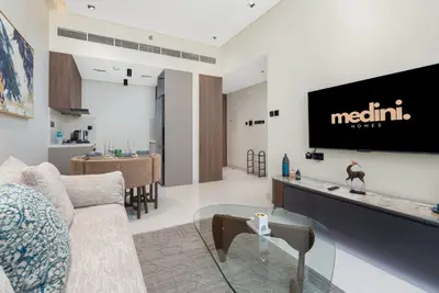 Living area with grey sofa, glass coffee table, kitchen bar, and wall-mounted TV