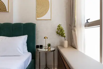Bedroom corner with a green velvet headboard, bedside lamp, and potted plant by the window
