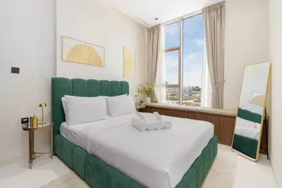 Bedroom with green velvet headboard, white bedding, folded towels, and city-view window