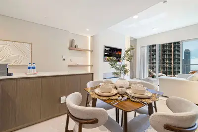 Dining area with round wooden table, upholstered chairs, and floor-to-ceiling city views
