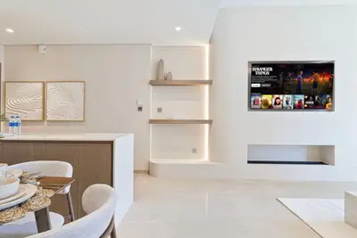 Open-plan area with wall-mounted TV, floating shelves, and dining table beyond