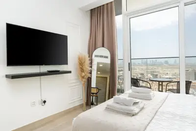 Bedroom corner showing wall-mounted TV, full-length mirror, and city view