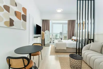 Open-plan studio with dining chairs, sofa, and floor-to-ceiling balcony window
