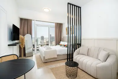 Studio living area with sofa, dining table, and sleeping zone beyond slatted divider
