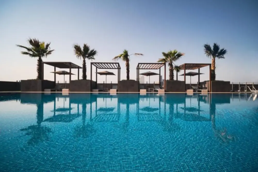 Rooftop pool with palm trees and shaded pergolas at dusk