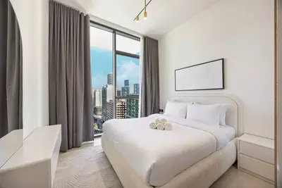 Bedroom with king bed, rolled towels and floor-to-ceiling window framing city buildings