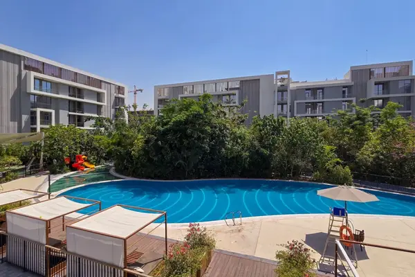 Outdoor pool with sun loungers surrounded by trees and low-rise buildings