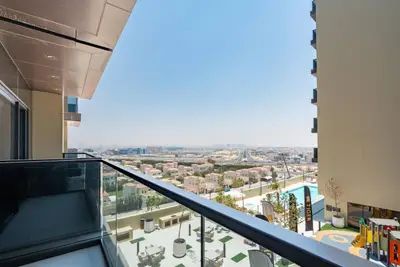 Balcony with glass railing overlooking a low-rise residential area and communal pool below