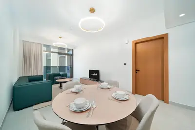 Dining area with round wooden table and grey chairs, living room beyond