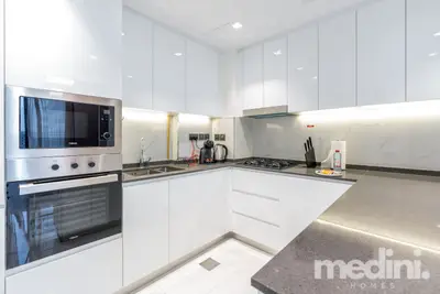 White gloss L-shaped kitchen with built-in oven, microwave and dark stone worktop