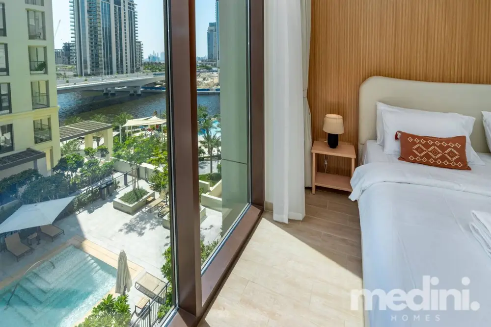 Bedroom corner with king bed beside open balcony door overlooking the creek and pool