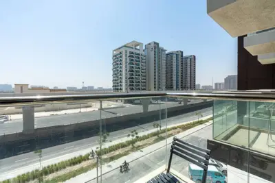Balcony with glass railing looking onto a boulevard and mid-rise blocks