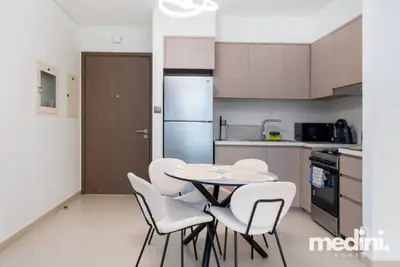 Dining area with round table and white chairs, kitchen with fridge behind