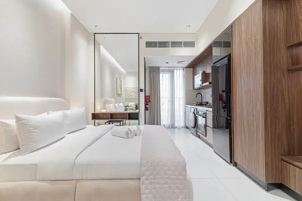 Studio with double bed, full-length mirror and open kitchen in warm white tones