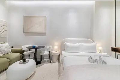 Open-plan studio showing the bed, green sofa and dining area in all-white decor