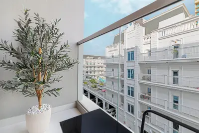 Balcony with a potted olive tree overlooking white apartment buildings across the street