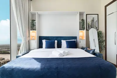 Double bed with blue velvet headboard, matching pillows and folded towels on white linen