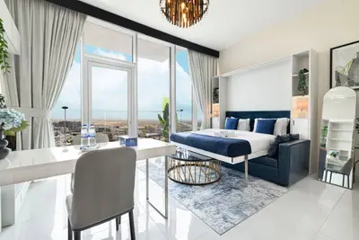 Open-plan studio with blue bed and floor-to-ceiling windows framing a wide city view