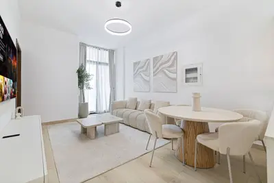 Living and dining area with round wooden table, linen chairs, and large window