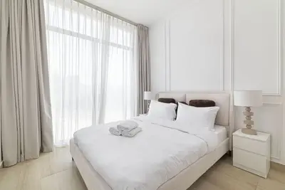 White bedroom with double bed, sheer curtains, and side lamp