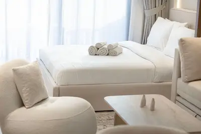 Bed with white linen and rolled towels, with cream sofa and coffee table visible