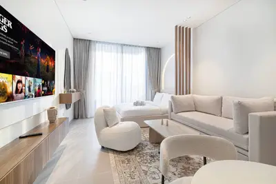Studio living area with sofa, TV, and bed visible through wooden partition screen