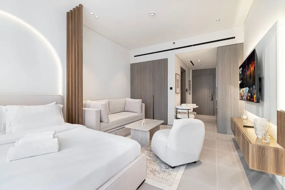 Full studio view showing bed, sofa, armchair, TV wall, and dining corner
