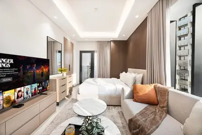 Studio from the sofa side showing the bed, TV unit, and balcony door