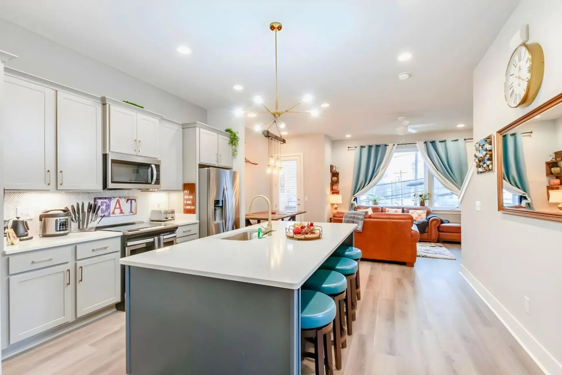 Open kitchen with white cabinetry, island with bar stools, stainless appliances, and living area