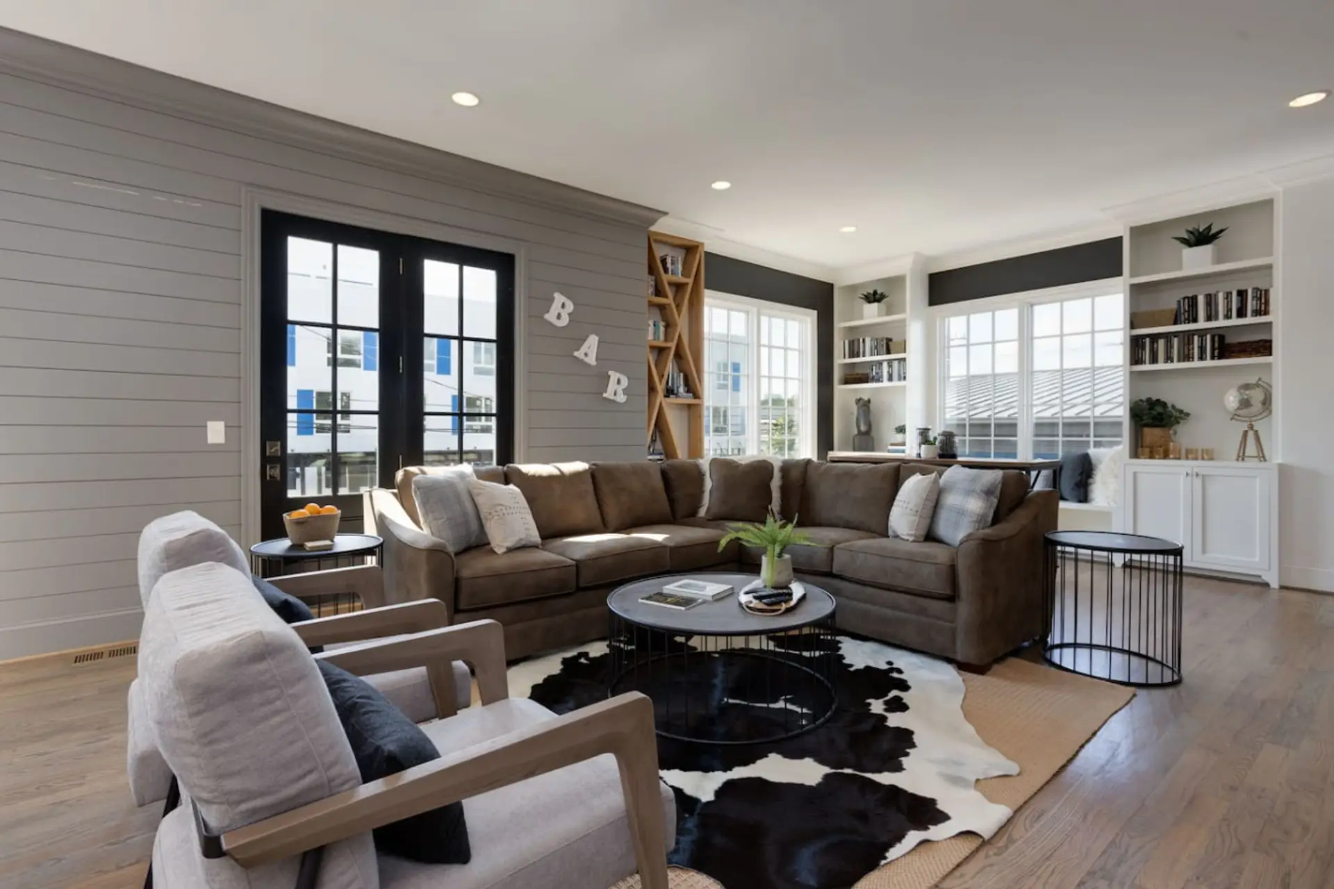 A spacious living room with a large sectional, built-in shelving, and tall windows creates an impressive first impression.