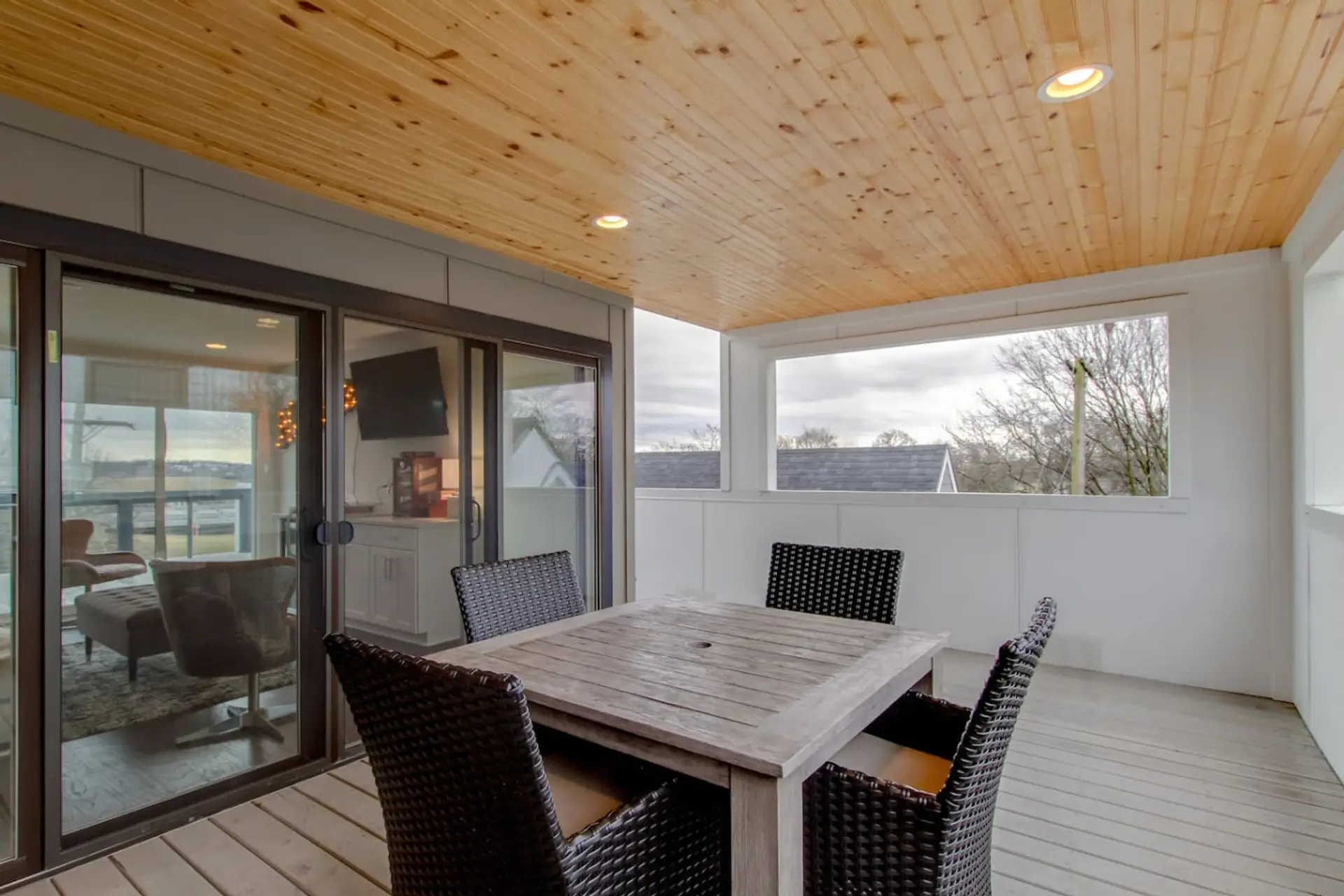 Rooftop deck with outdoor dining table, wicker chairs, and wood-paneled ceiling