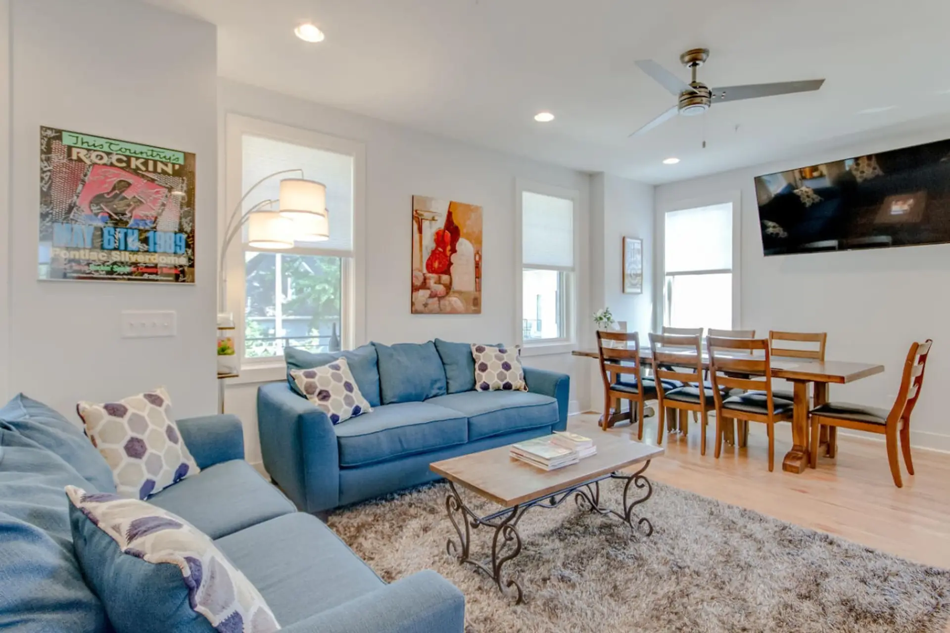 Open living and dining area with a blue sofa, ceiling fan, wall art, and dining table