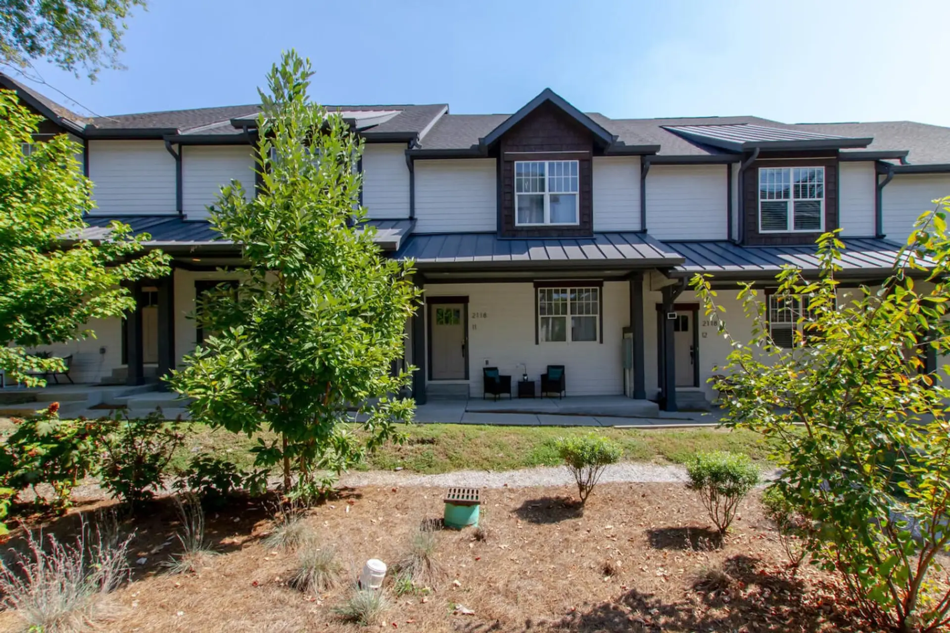 Exterior of two-story craftsman home with dark facade, green trees, and landscaped garden
