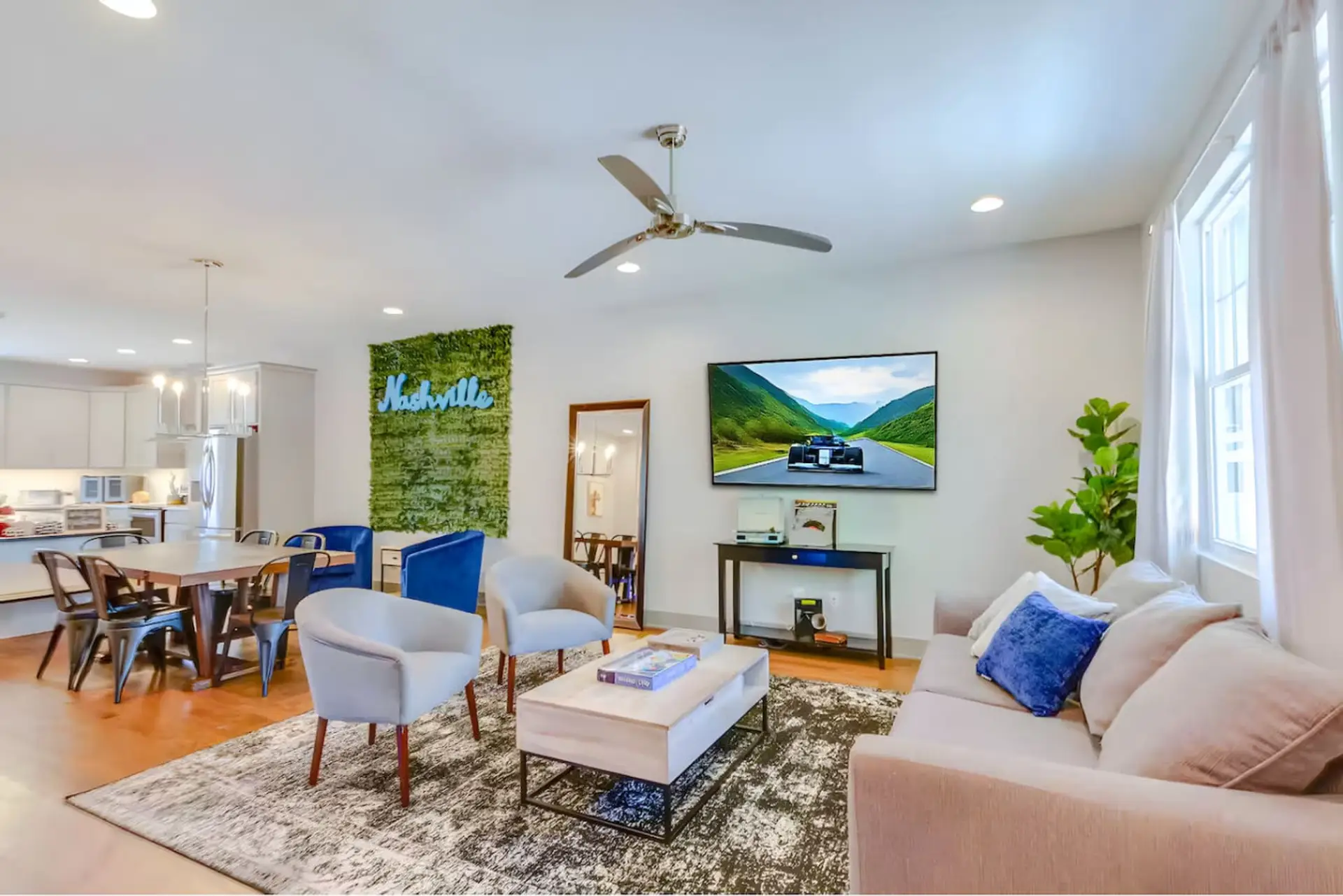 Living room with cream sofa, blue accent pillows, green wall art, TV, ceiling fan, and area rug