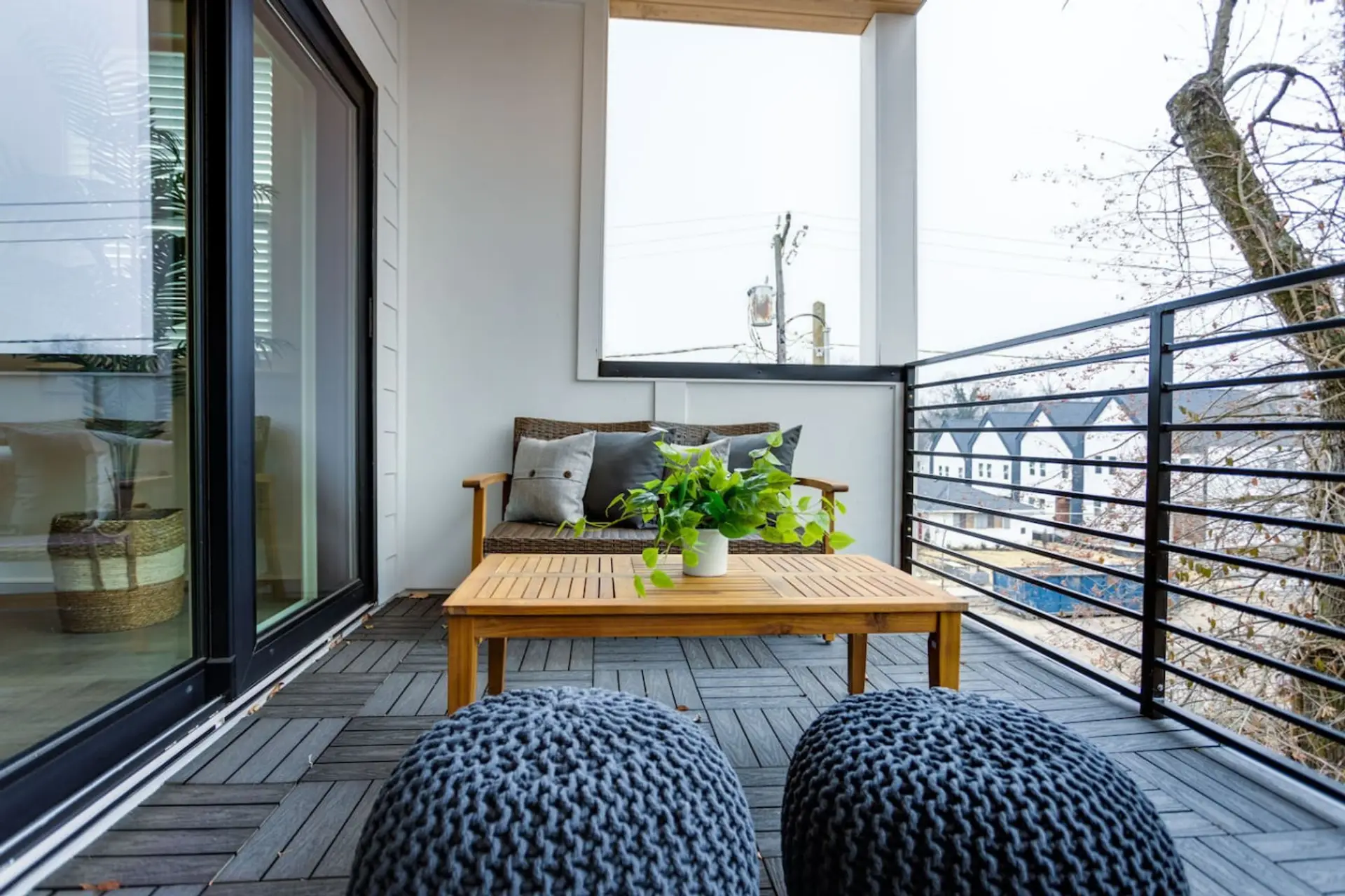 Balcony patio with outdoor sofa, wood coffee table, and wicker ottoman poufs