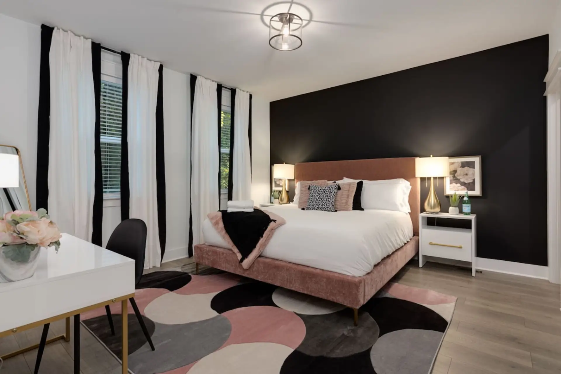 Bedroom with pink upholstered headboard, white bedding, geometric rug, and tall windows