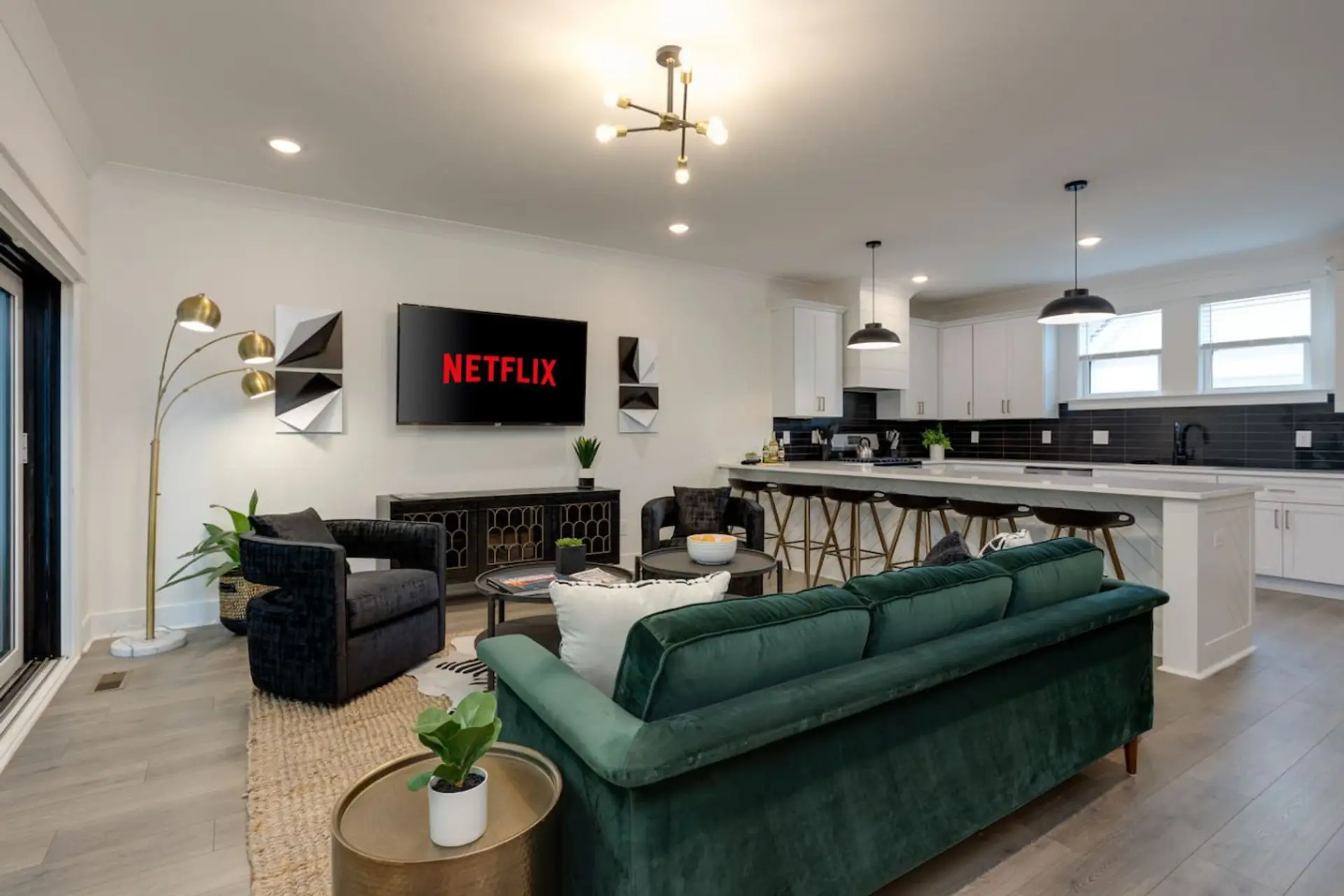Living room with emerald green velvet sofa, Netflix display, kitchen island, and pendant lights